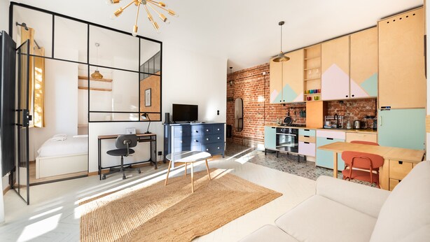 A modern living room with a sofa, a dining table, and a kitchen area with colorful cabinets and a brick wall. - Saska Kępa Loft Style Apartment (Warszawa)