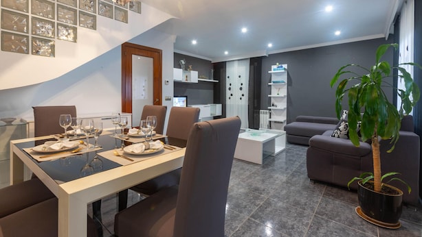 A modern living room with a dining area, a staircase, and a potted plant. - Charming House in Roses, Costa Brava: Private Pool, Close to the Beach, Ideal for Families and Groups. (Roses)