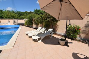 A poolside area with lounge chairs and a large umbrella. - Charming House in Roses, Costa Brava: Private Pool, Close to the Beach, Ideal for Families and Groups. (Roses)