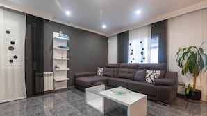 A modern living room with a sectional sofa, a glass coffee table, a white shelving unit, and a potted plant. - Charming House in Roses, Costa Brava: Private Pool, Close to the Beach, Ideal for Families and Groups. (Roses)
