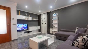 A modern living room with a flat-screen TV, a glass coffee table, a grey sofa, and a white entertainment unit. - Charming House in Roses, Costa Brava: Private Pool, Close to the Beach, Ideal for Families and Groups. (Roses)