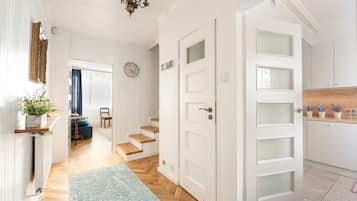 Ein Flur mit Holzboden, einem blauen Teppich, einer weißen Tür mit geätzten Glasscheiben und einer Treppe, die in ein weiteres Zimmer führt.