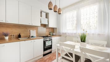 Eine moderne Küche mit weißen Schränken, einer Holzauskładung, einem Herd und einem Essbereich mit weißen Stühlen und einem Tisch.