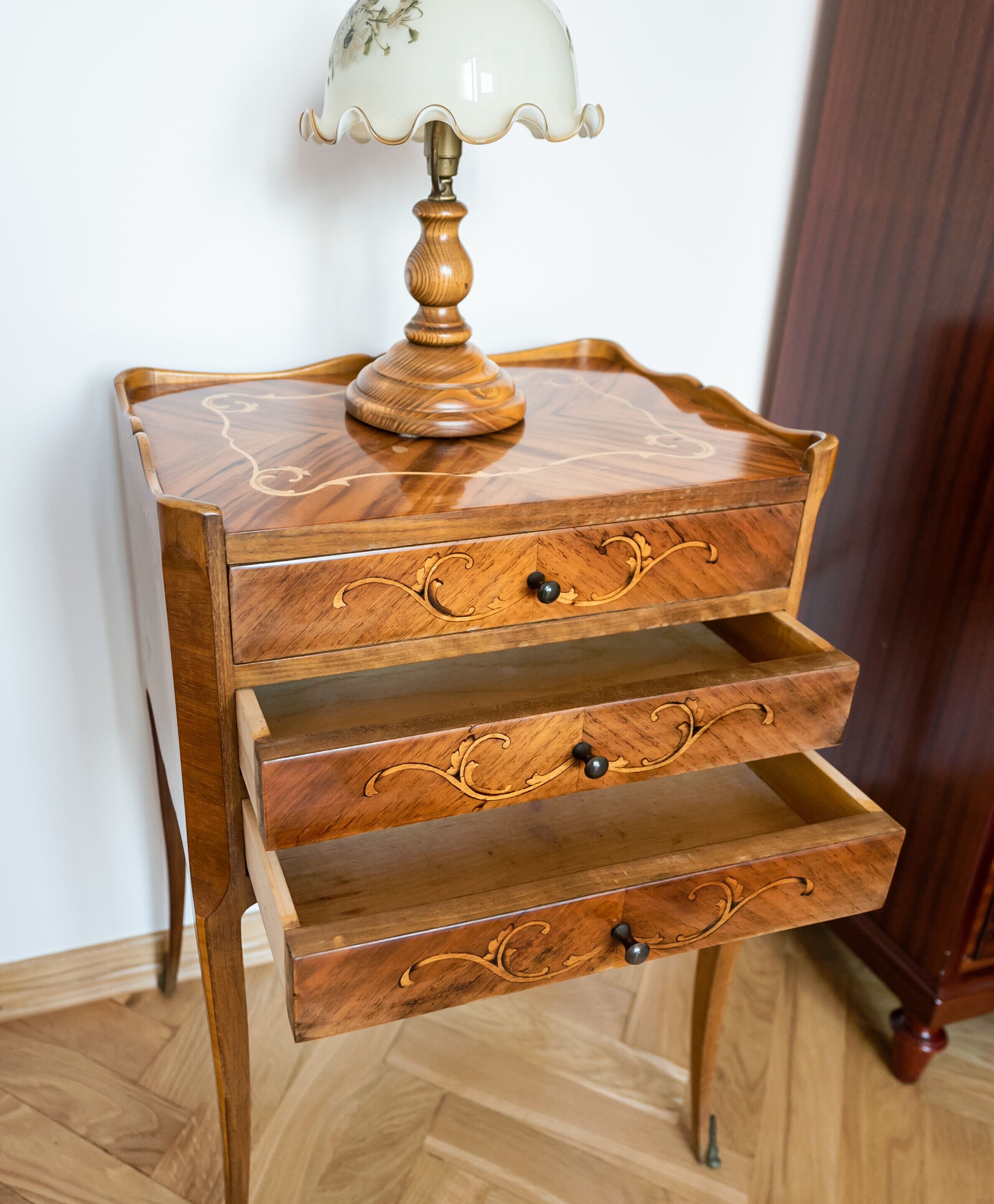 Une table de chevet en bois, avec une lampe, des tiroirs et un petit plateau.