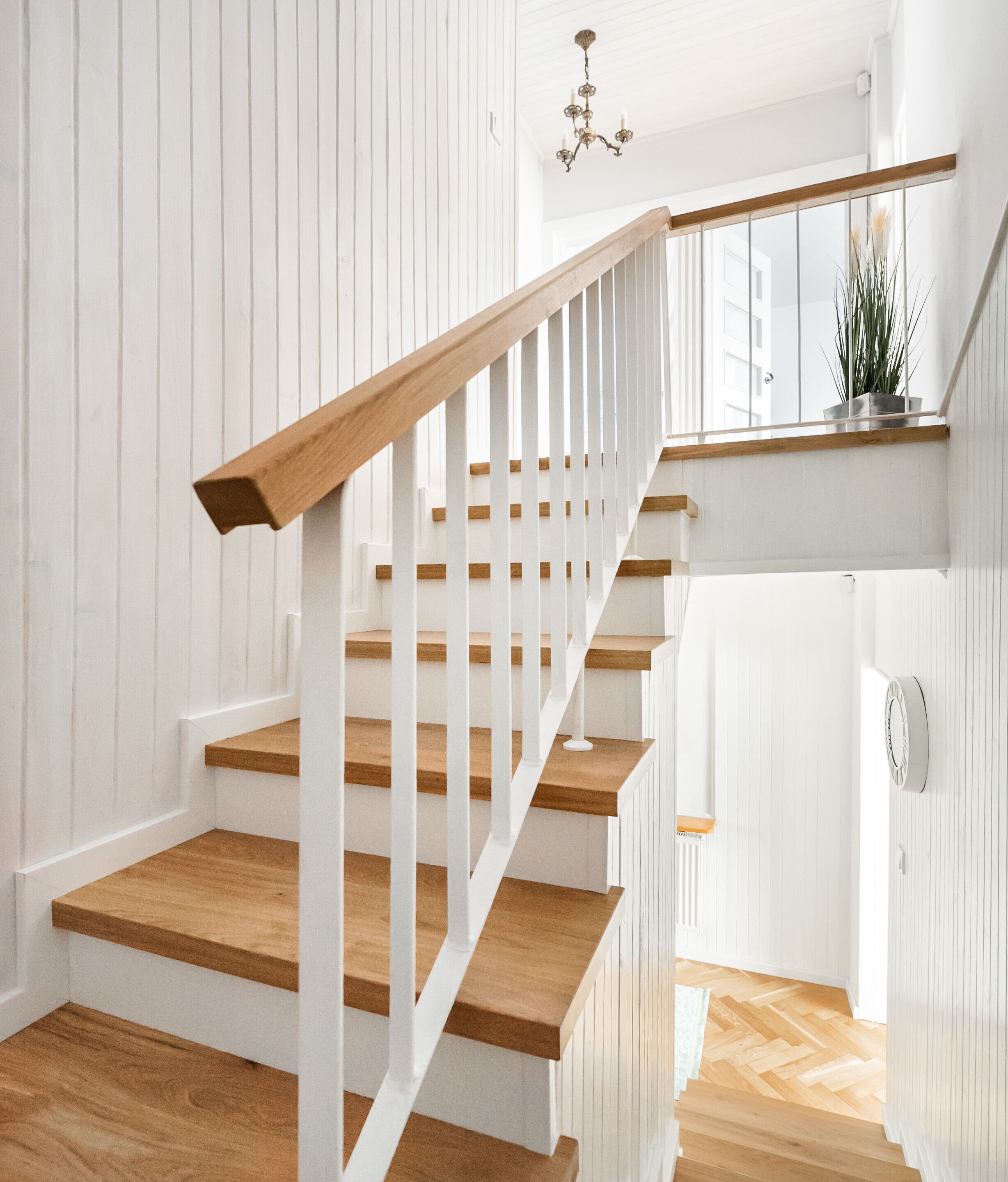 A staircase with wooden steps and white railings, leading to a landing with a potted plant.