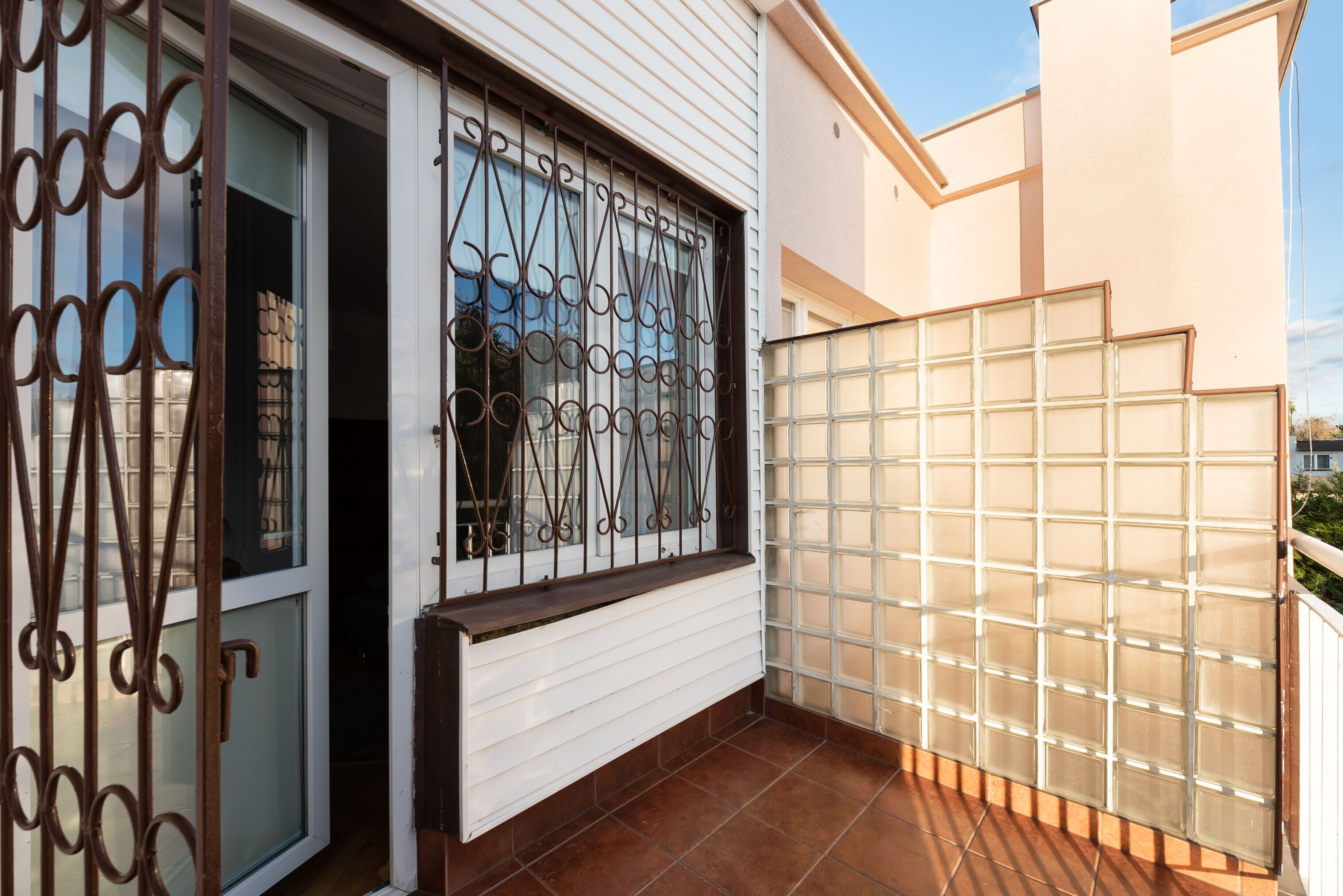 Un balcon avec un mur extérieur blanc, une fenêtre ornée de barreaux en fer forgé et une clôture en blocs de verre.