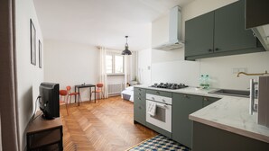 Cocina compacta con piso de espiga, estufa a gas, un lavamanos y un pequeño comedor con dos sillas.