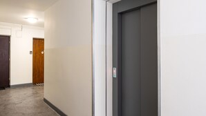 Un pasillo con piso alfombrado, una puerta de madera y una puerta de ascensor gris.