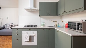 Una cocina moderna con estufa, horno y microondas integrados, con armarios verdes y encimera blanca.