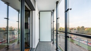 A narrow balcony with large glass doors leading to a room, offering a view of a busy road and distant buildings. - New Varsovia Comfort 310 (Warszawa)