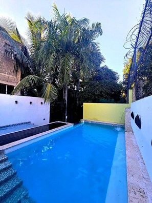 A swimming pool with steps leading into it, surrounded by palm trees and a building with a yellow wall. - Hotelito Bonito Eli & Edw (Santo Domingo)