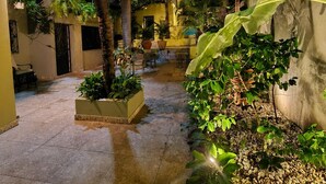 Une cour intérieure dotée d’un sol carrelé, de plantes en pot et d’un espace détente avec des tables et des chaises.
