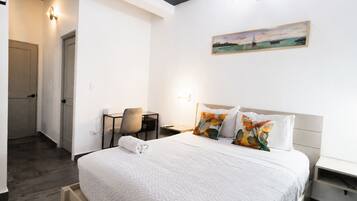 A hotel room with a bed, a desk, a chair, a painting, and a door.