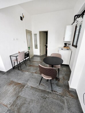 Een moderne keuken met een eethoek, met een ronde zwarte tafel en twee stoelen, een klein aanrecht met een spoelbak, en uitzicht op de aangrenzende kamer.