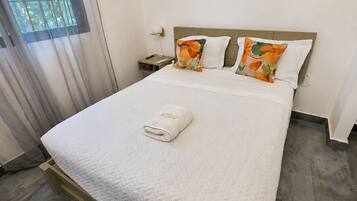 Uma cama bem arrumada com um edredom branco, cabeceira de madeira e travesseiro estampado com flores.