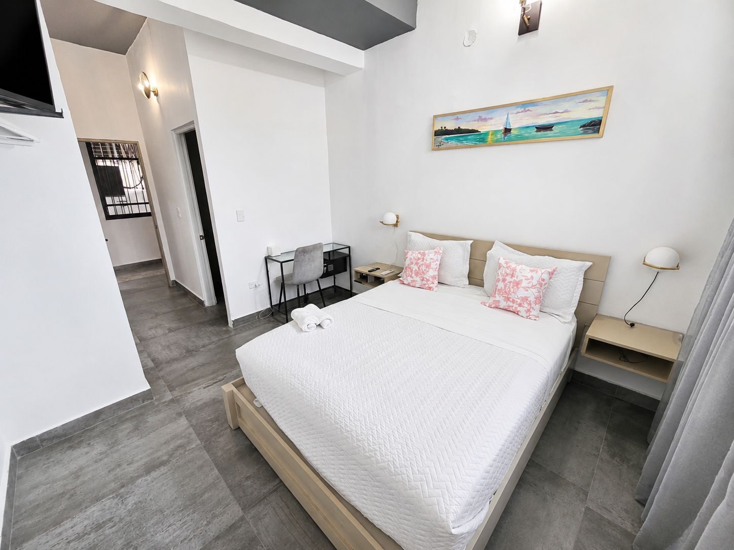 A modern hotel room with a large bed, a desk, and a painting on the wall.