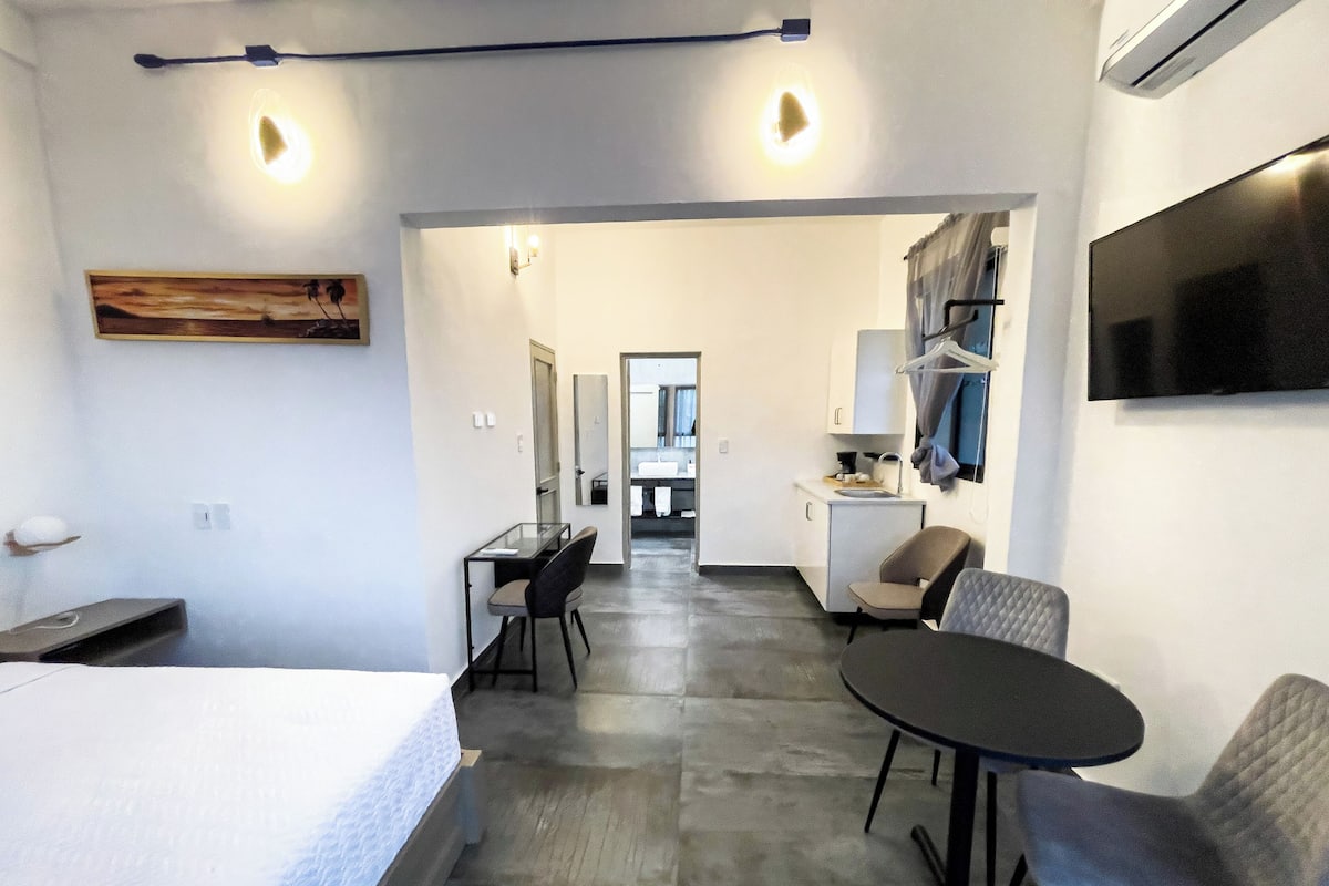 Een moderne hotelkamer met een bed, een bureau, een stoel en een klein tafeltje. Er is een televisie aan de muur bevestigd en een schilderij.