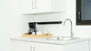 Une cuisine moderne avec des meubles blancs, un évier en acier inoxydable et une machine à café posée sur un plateau en bois.
