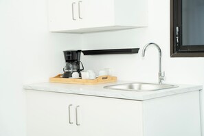 Een moderne keuken met witte kasten, een roestvrijstalen spoelbak en een koffiezetapparaat op een houten dienblad.