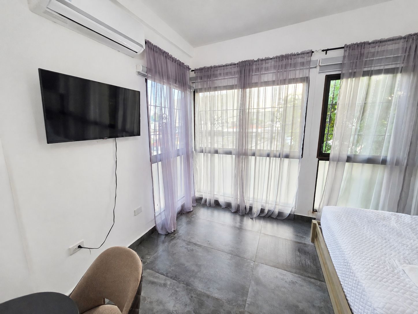 Hotellihuone, jossa on seinälle asennettu taulutelevisio, valkoisella peitteellä varustettu sänky ja tuoli.