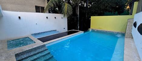 A swimming pool with steps leading into it, surrounded by walls and greenery.