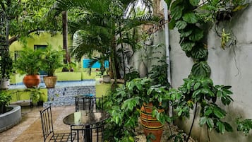 Un patio al aire libre con una mesa redonda y sillas, rodeado de exuberante follaje y plantas en macetas.