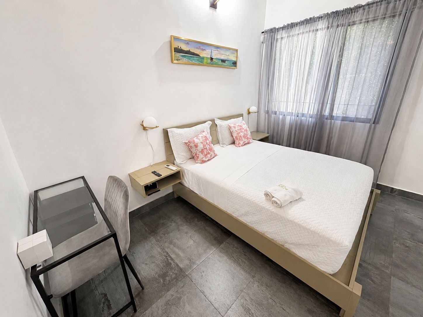 A hotel room with a bed, bedside table, lamp, chair, and a painting on the wall.