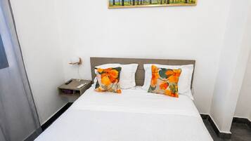 A hotel room with a bed, a painting on the wall, and an air conditioning unit.