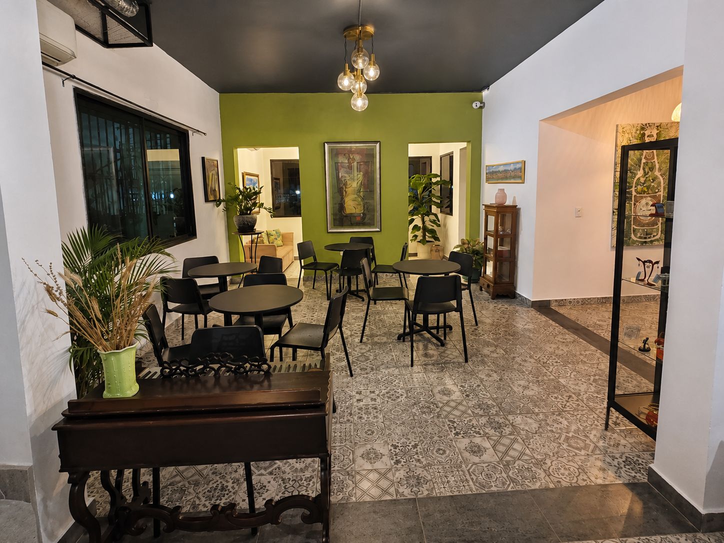 Un espace repas avec des tables et des chaises rondes, un mur d’accent vert et un luminaire au plafond.