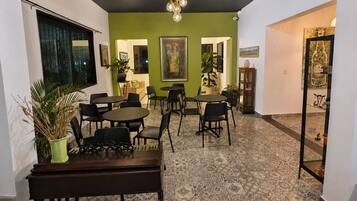 Un espace repas avec des tables et des chaises rondes, un mur d’accent vert et un luminaire au plafond.