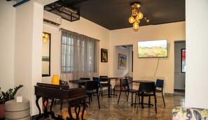 A hotel lobby with a dining area, a large TV screen, and a ceiling fan. - Hotelito Bonito Eli & Edw (Santo Domingo)