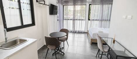 A compact hotel room with a kitchenette, a bed, a small dining table, and a TV mounted on the wall.