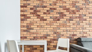 Una habitación con pared de ladrillo, una mesa blanca con dos sillas, un sofá gris y una alfombra pequeña.
