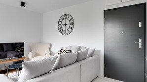 Una sala de estar moderna con un sofá gris, un reloj de pared con marco negro y una puerta cerrada.