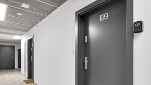 Un pasillo con una puerta gris oscura con la etiqueta 199, paredes blancas y piso de baldosas.