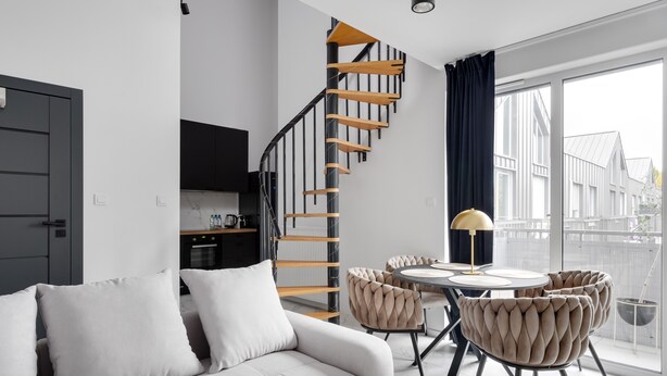 Una sala de estar moderna con un sofá, una mesa de comedor con sillas, una escalera y vistas al exterior.