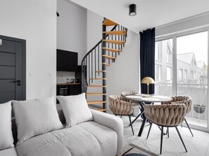 Una sala de estar moderna con un sofá, una mesa de comedor con sillas, una escalera y vistas al exterior.