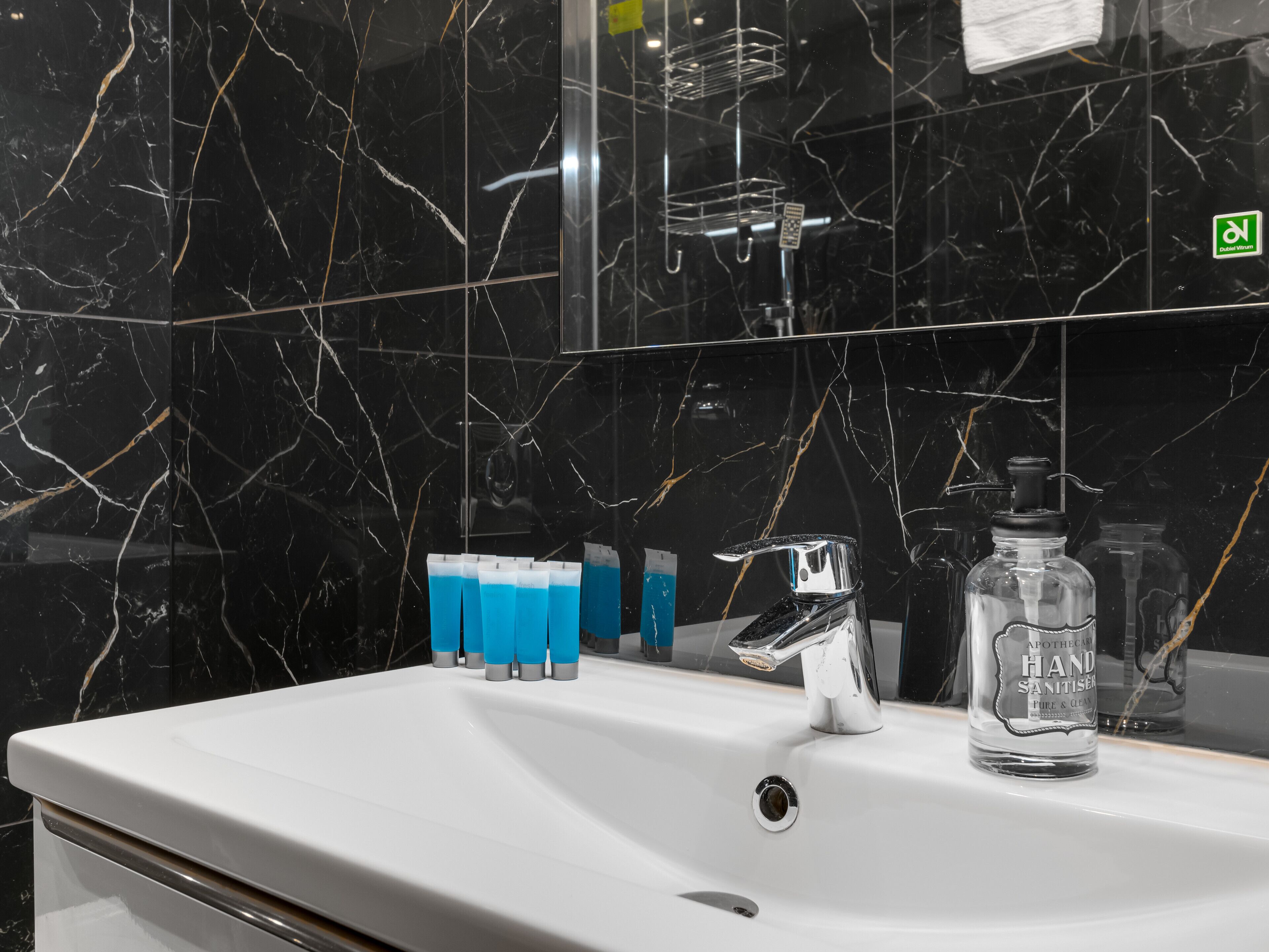 A bathroom with a white sink, a mirror, and black marble walls.