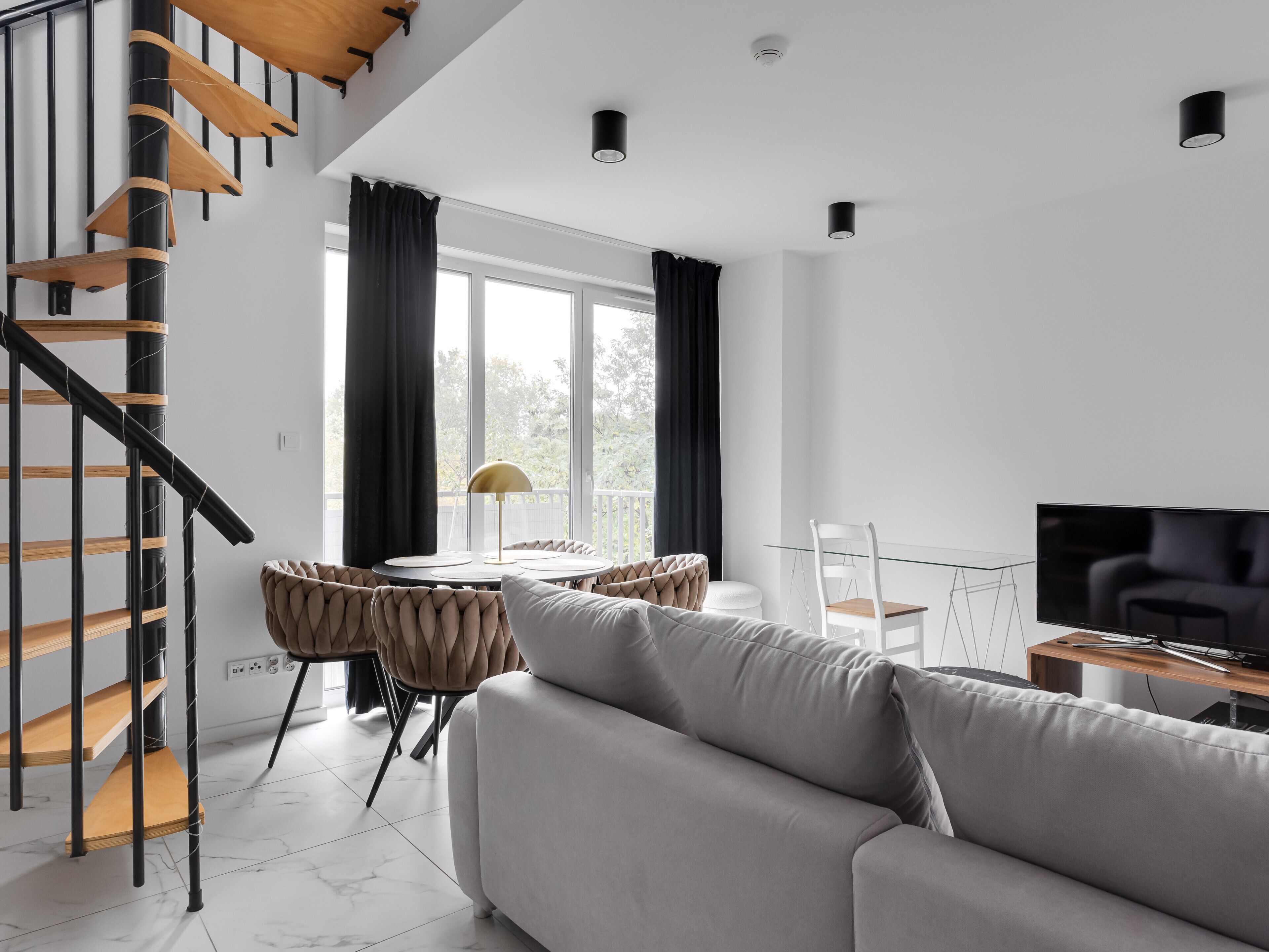 A modern living room with a staircase, a sofa, a dining table with chairs, and a TV.