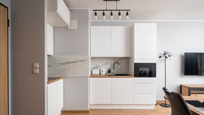 A modern kitchen with white cabinets, a marble countertop, and a black microwave. - Wiktoryn Comfortable Two-Room Apartment (Warszawa)