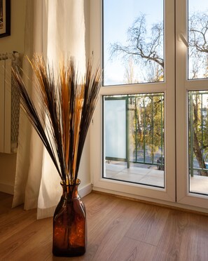 A room with a large window, a vase with tall reeds, and a wooden floor.