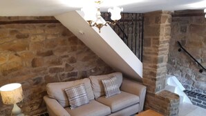 Un salon chaleureux avec un mur en pierre, un ensemble de canapés, une table basse en bois et un escalier.