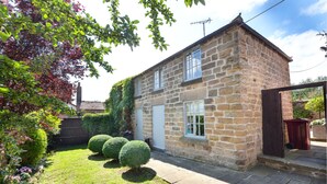 Une maison en pierre avec un jardin, une porte blanche et une fenêtre à cadre blanc.