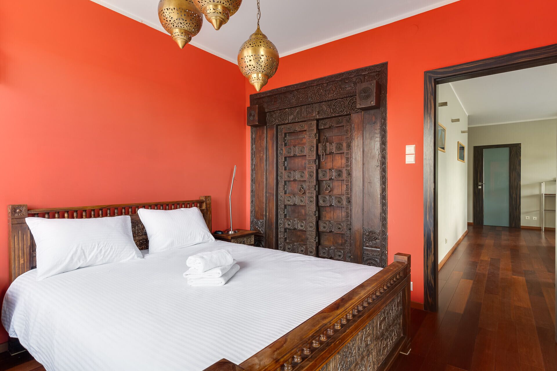 Una habitación con una cama, una puerta de madera con intrincados grabados y un pasillo.