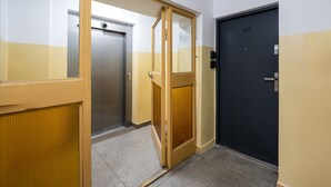 A hallway with a closed elevator, a door with a number plate, and a wall with a color pattern. - Służew 405A Apartment (Warszawa)