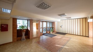 A spacious lobby with a tiled floor, a reception desk, potted plants, and a view through a glass door. - Służew 405A Apartment (Warszawa)