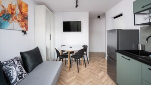 A modern kitchen with a built-in fridge, a dining area with a table and chairs, and a grey sofa with black cushions. - Służew 405A Apartment (Warszawa)