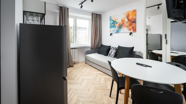 A modern kitchen with a refrigerator, a dining table with chairs, a sofa with cushions, and a window with curtains. - Służew 405A Apartment (Warszawa)
