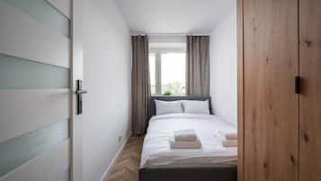 Un dormitorio con cama, armario, ventana con cortinas y una planta.