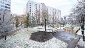 Un parque cubierto de nieve con un área de juegos, un edificio grande de varios pisos y algunos árboles.